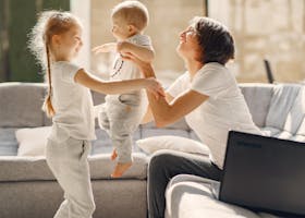 Side view of smiling woman playing with toddler boy and girl while sitting on sofa in living room
