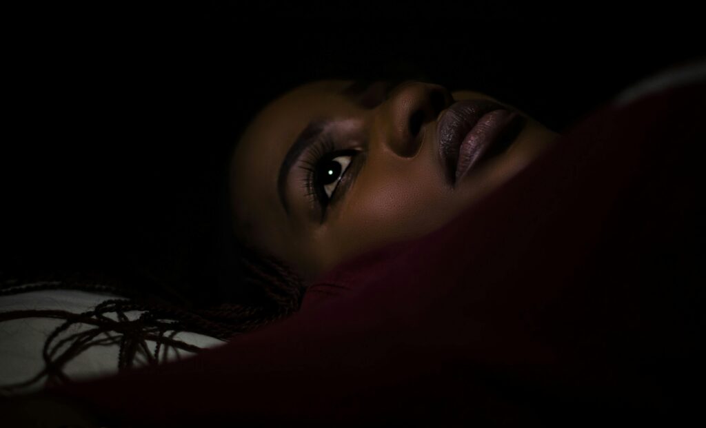 Close-up shot of a woman lying down in a dark, intimate setting.